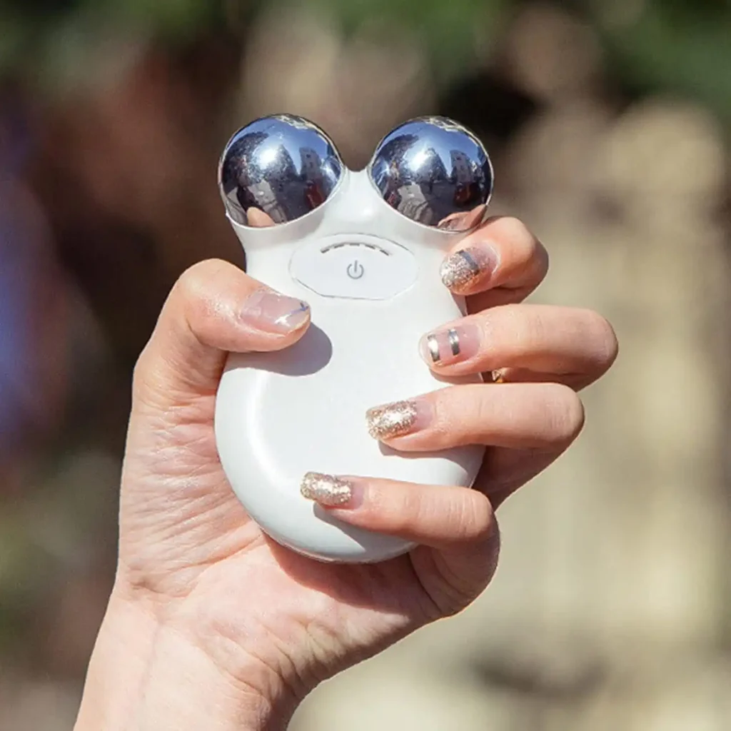 Hand holding the facial toning device outdoors showing portable design and sleek finish